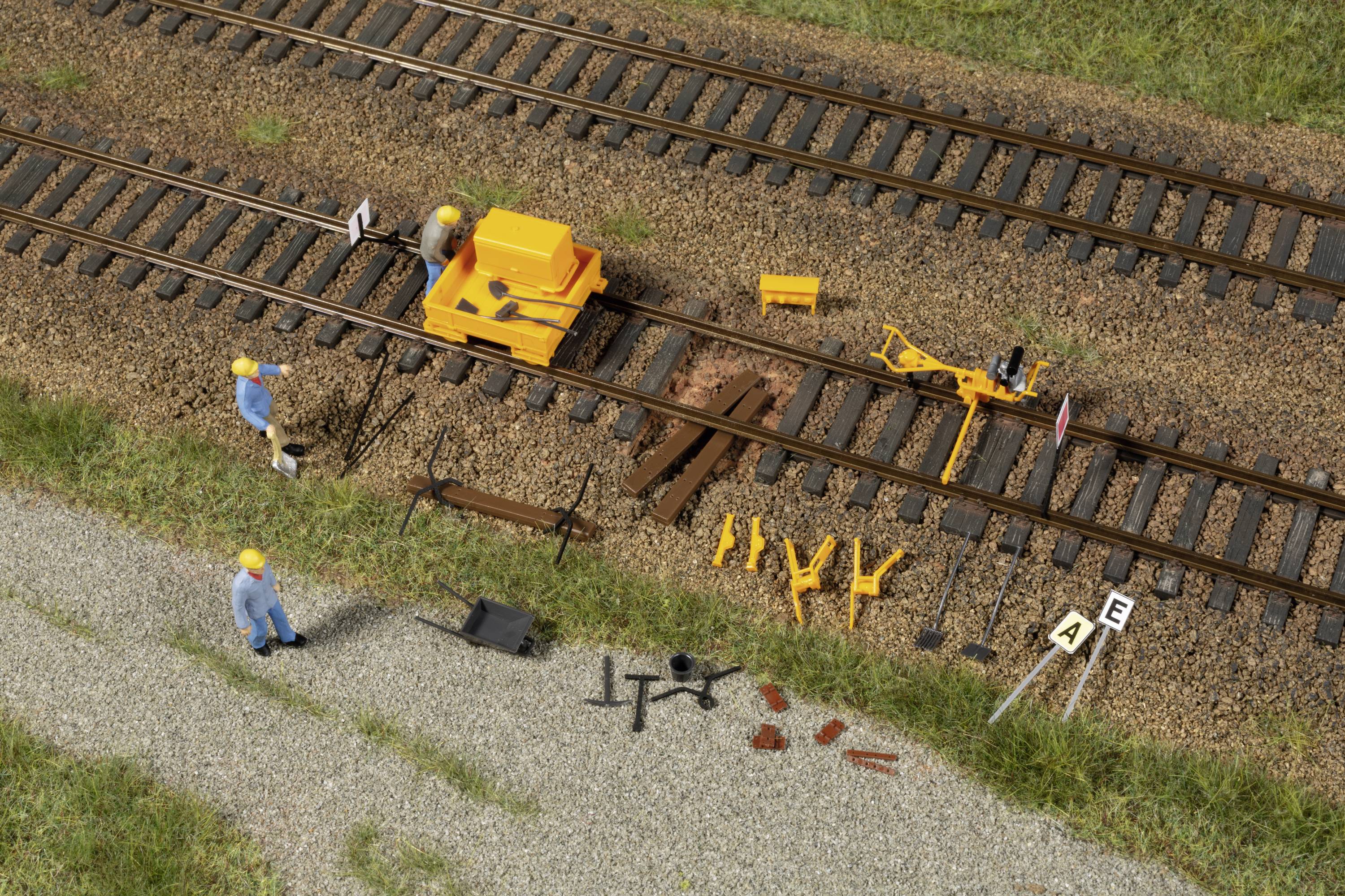 Construction workers are repairing rails on a railway line. A yellow machine is in operation. Tools and materials are laid out ready.