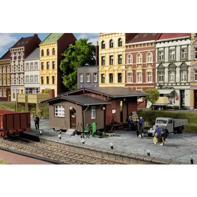Model railway diorama depicting a goods station with loading bay and warehouse. People at work, surrounded by urban buildings.