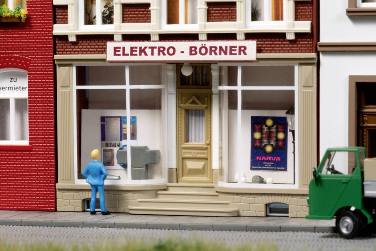 A miniature model of an electrical shop with the sign 'ELEKTRO - BÖRNER'. A person is standing in front of it, a green car is on the right.