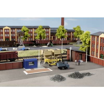 A miniature railway scene with industrial buildings, a lorry, two figures and tracks with goods wagons standing on them.