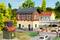 'Model landscape with a small railway station, passing cars and pedestrians. Houses and trees are visible in the background.'