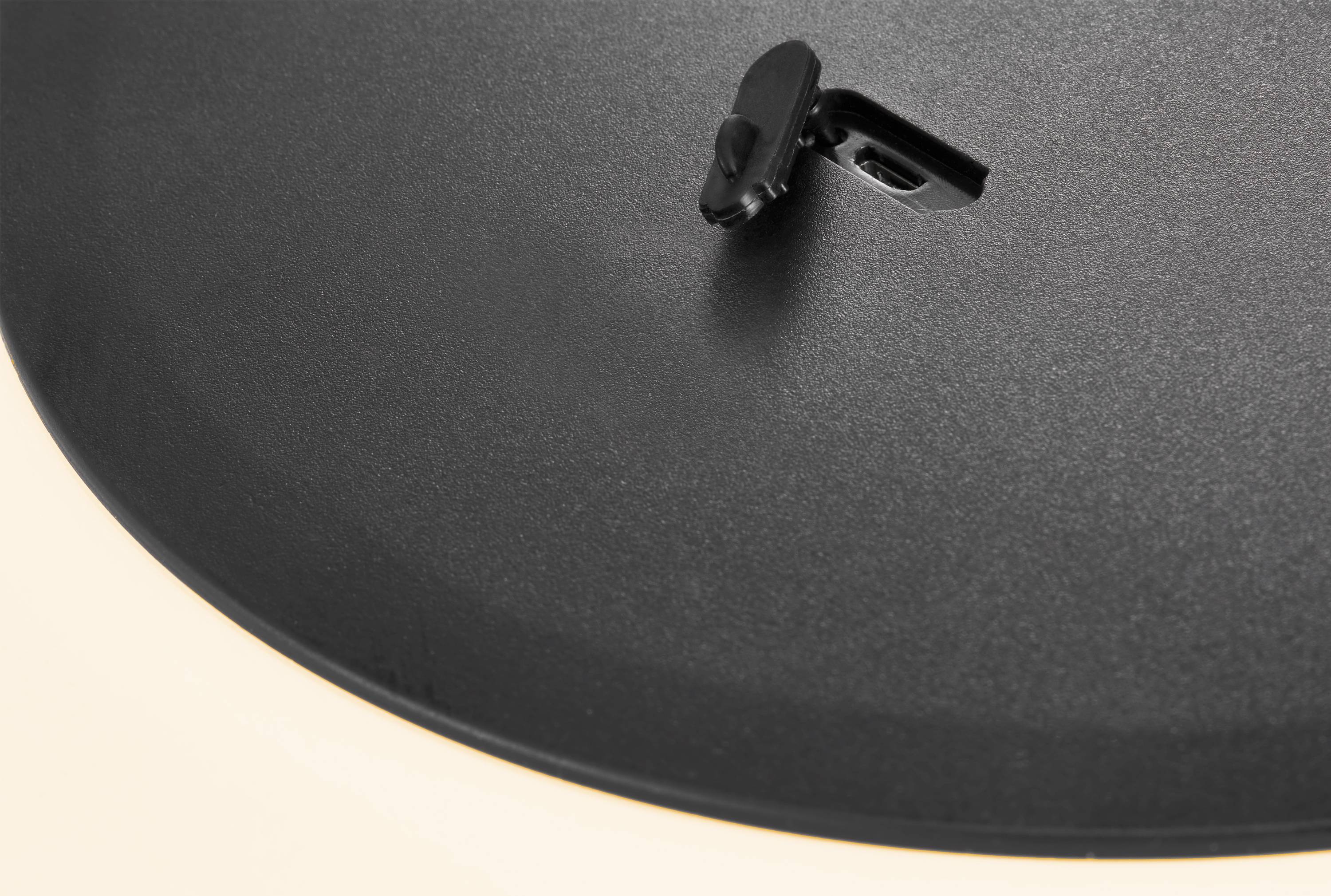 A black saucepan lid with a slightly ajar fastening sits on a pot. The lid has a smooth, matte surface.