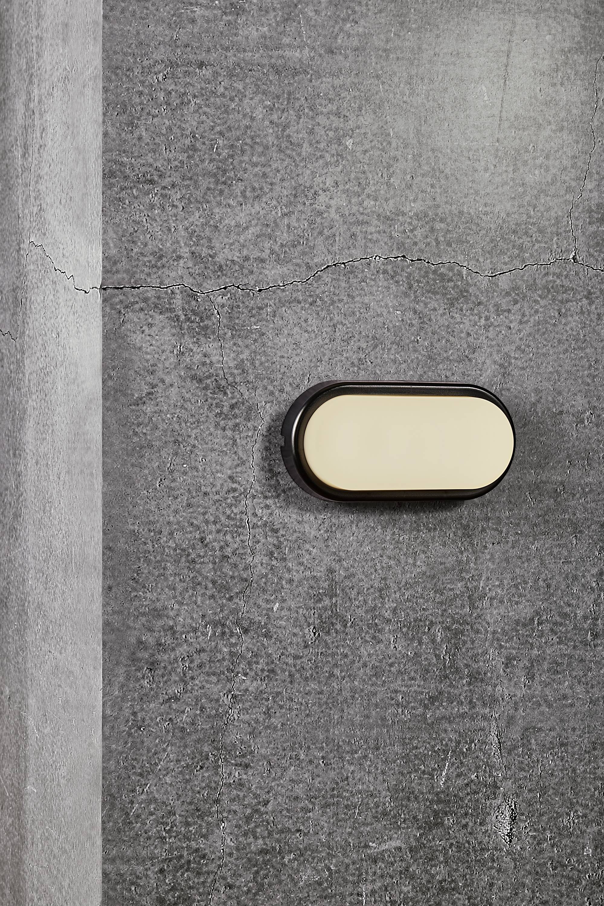 An oval wall light with a cream-coloured shade mounted on a grey, textured concrete wall.