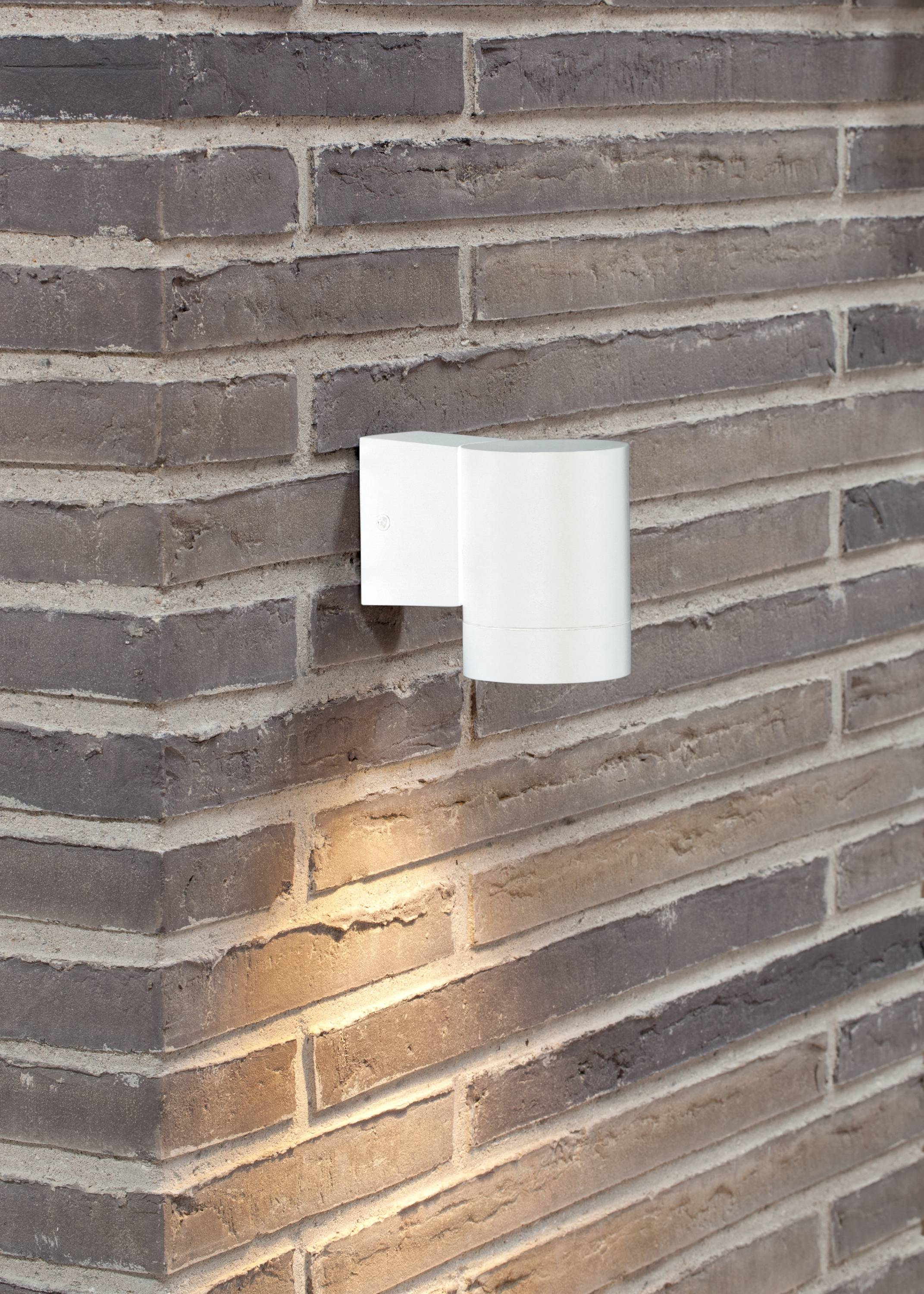 White wall light on a brick wall, casting downward and illuminating the wall with warm light.