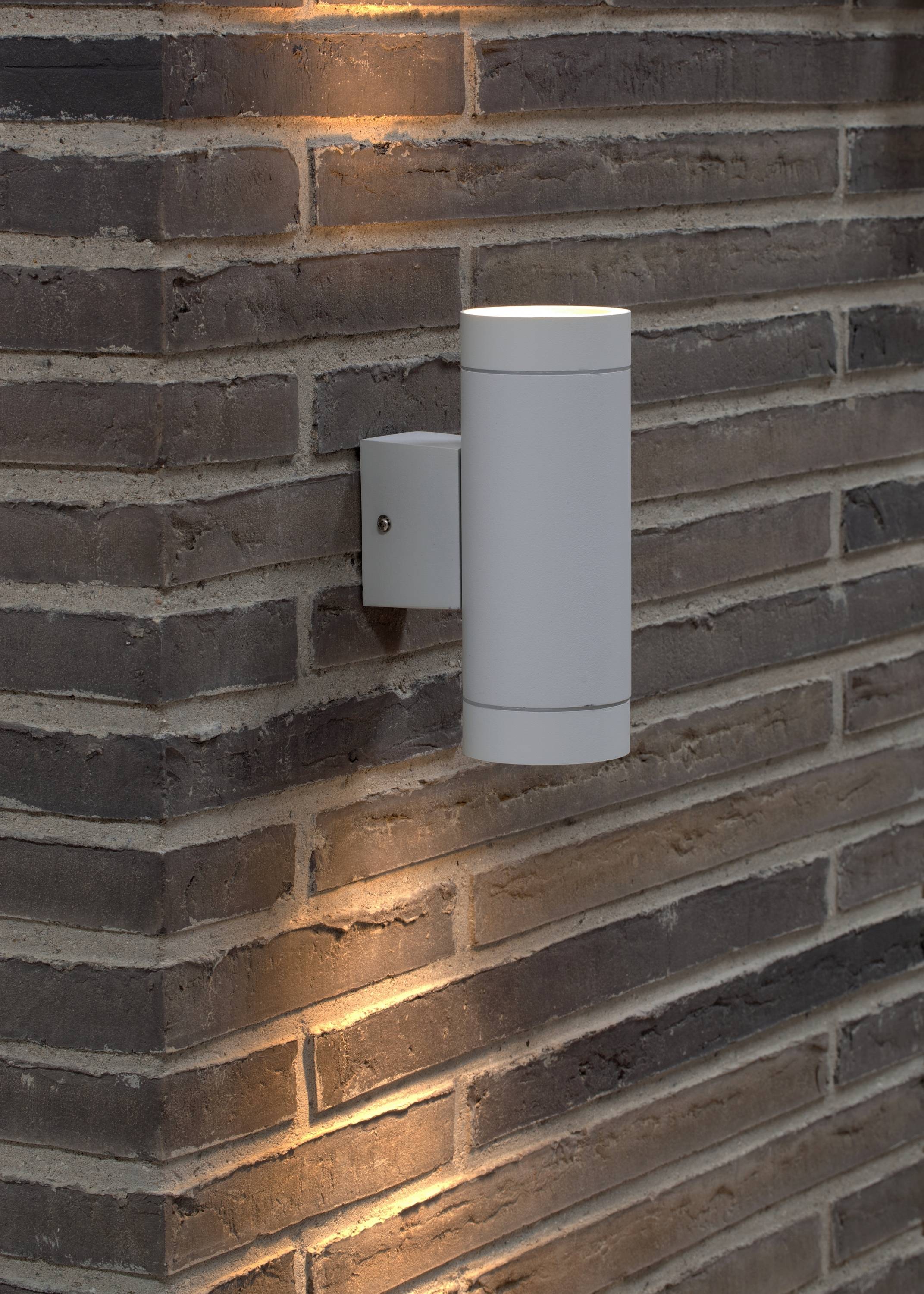 A modern outdoor light on a brick wall, casting warm light upwards and downwards, highlighting the texture of the brickwork.