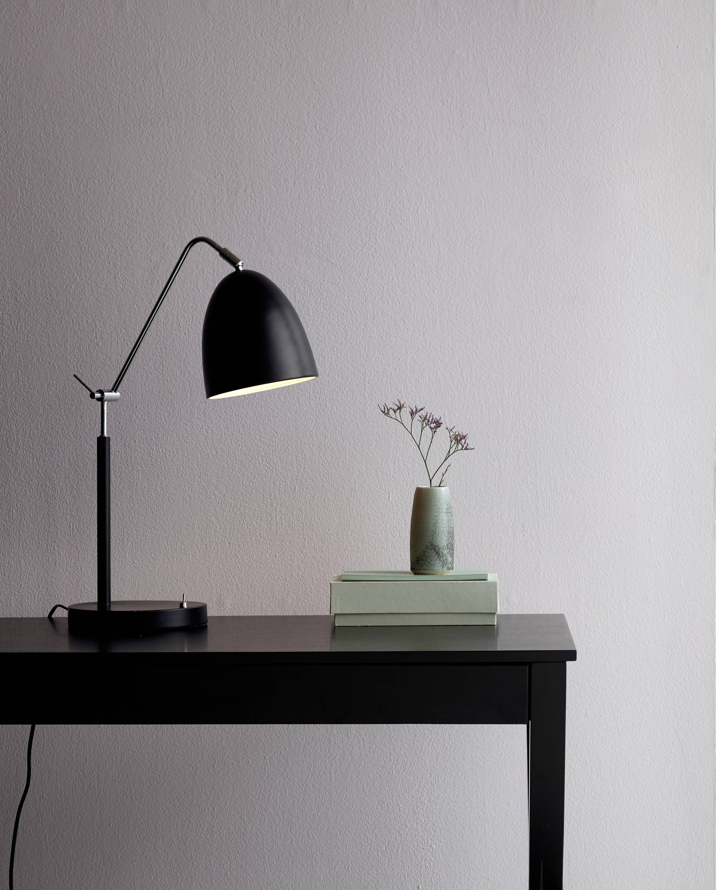 Black table lamp on a dark table next to a small vase with flowers, minimalist and stylish design.