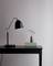 Black table lamp on a dark table next to a small vase with flowers, minimalist and stylish design.