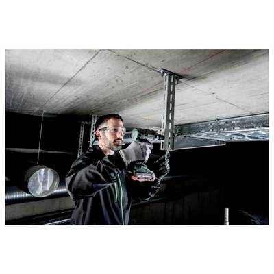 A person wearing safety glasses and gloves uses a power drill to install ceiling supports in an industrial setting.