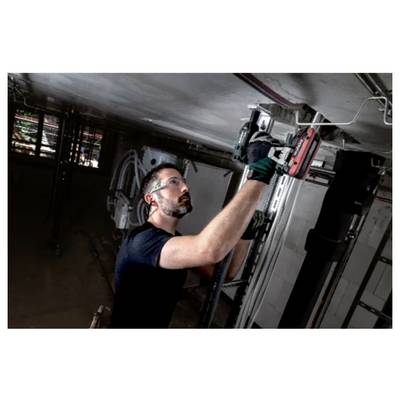 A man wearing safety goggles and gloves uses a power tool while standing on a platform, working on a ceiling structure in an industrial setting.
