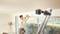 A man is using a green laser spirit level, which is attached to a ladder, to mount curtains above a large window.