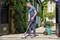 A man is cleaning the paving with a pressure washer in front of a house surrounded by plants. Green gas bottles are visible in the background.