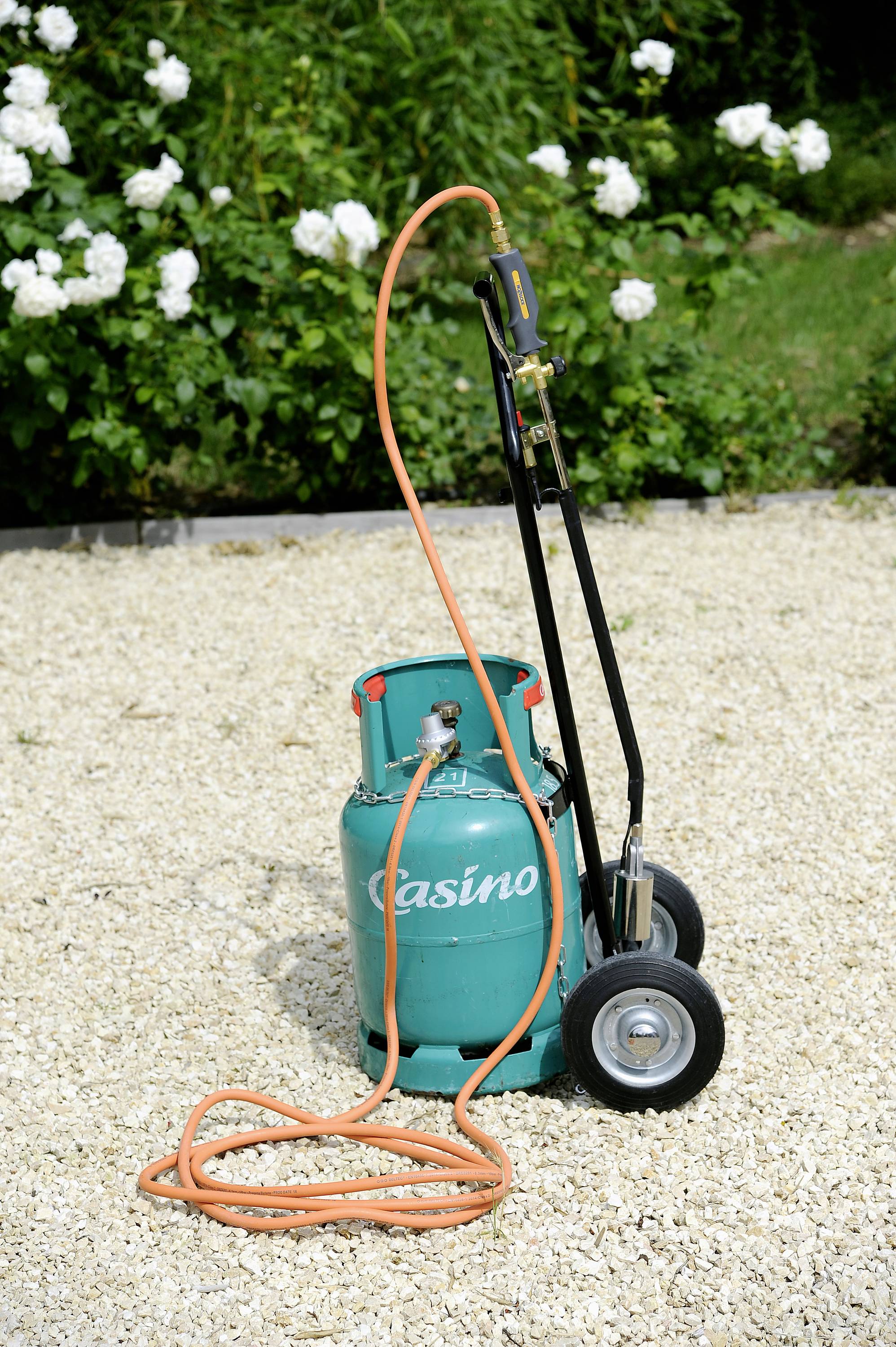 Gas bottle with hose and burner on a trolley, positioned on a gravel path, suitable for garden or construction work.