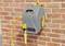 Grey hose reel with yellow garden hose, mounted on a red brick wall. Crank on the side for winding up the hose.