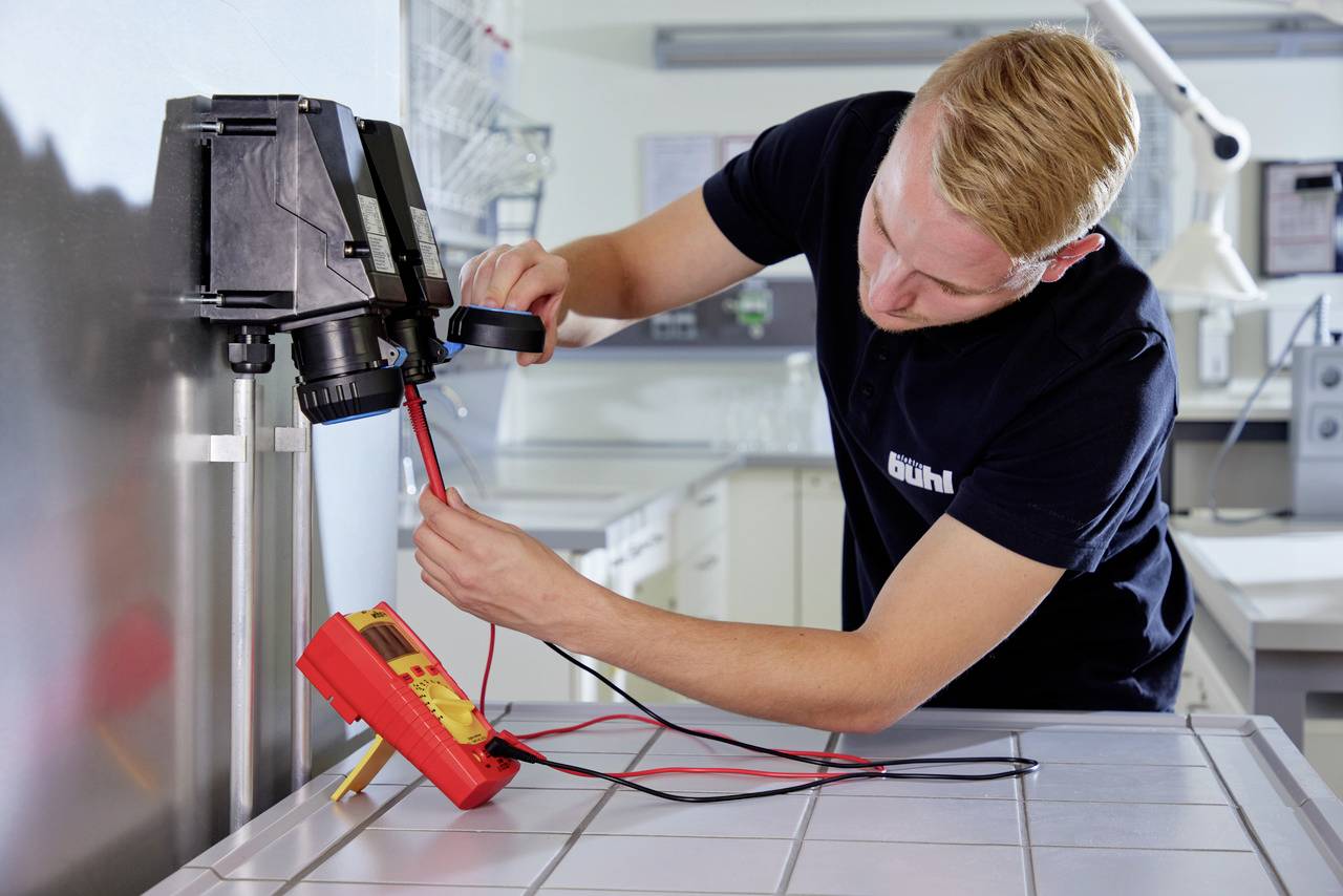 A man is working in a laboratory, testing electrical connections with a multimetre. He is measuring the resistance on a device.