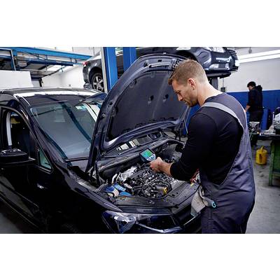 A mechanic in a garage is checking a car's engine using a diagnostic device. Other cars can be seen in the background.
