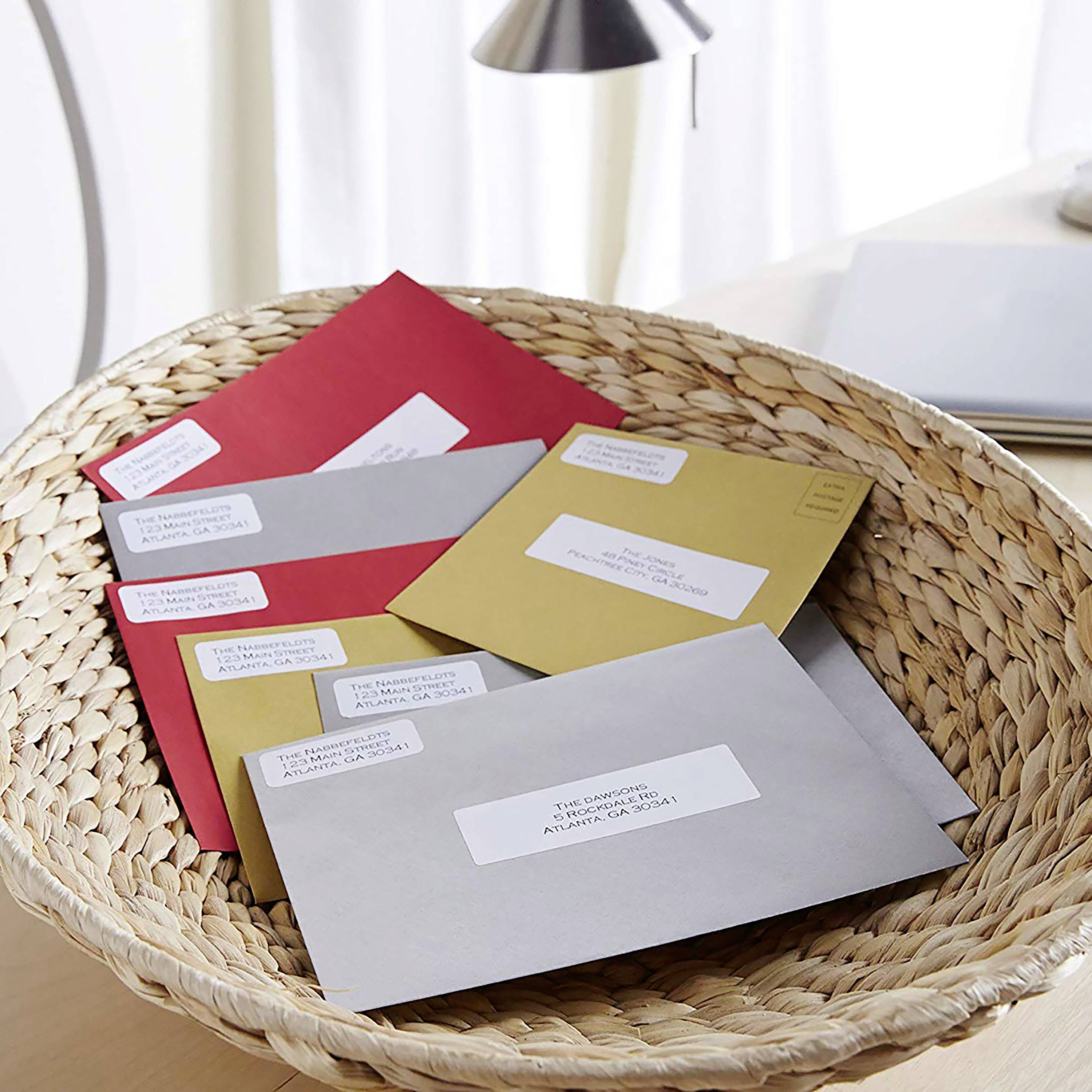 A basket containing several envelopes, some grey, some red, some with address labels. The basket is sitting on a light-coloured table.