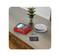 A smoke detector lies beside its packaging and instruction manual on a wooden table. A small plant is positioned nearby.