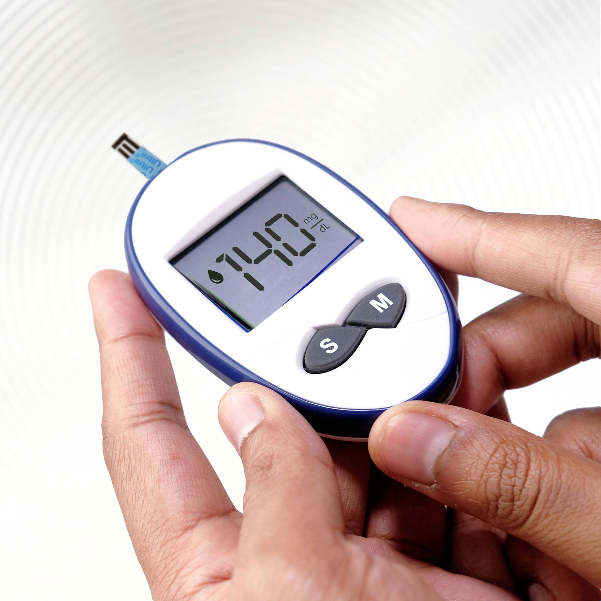 A person is holding a blood glucose metre showing '140 mg/dL'.