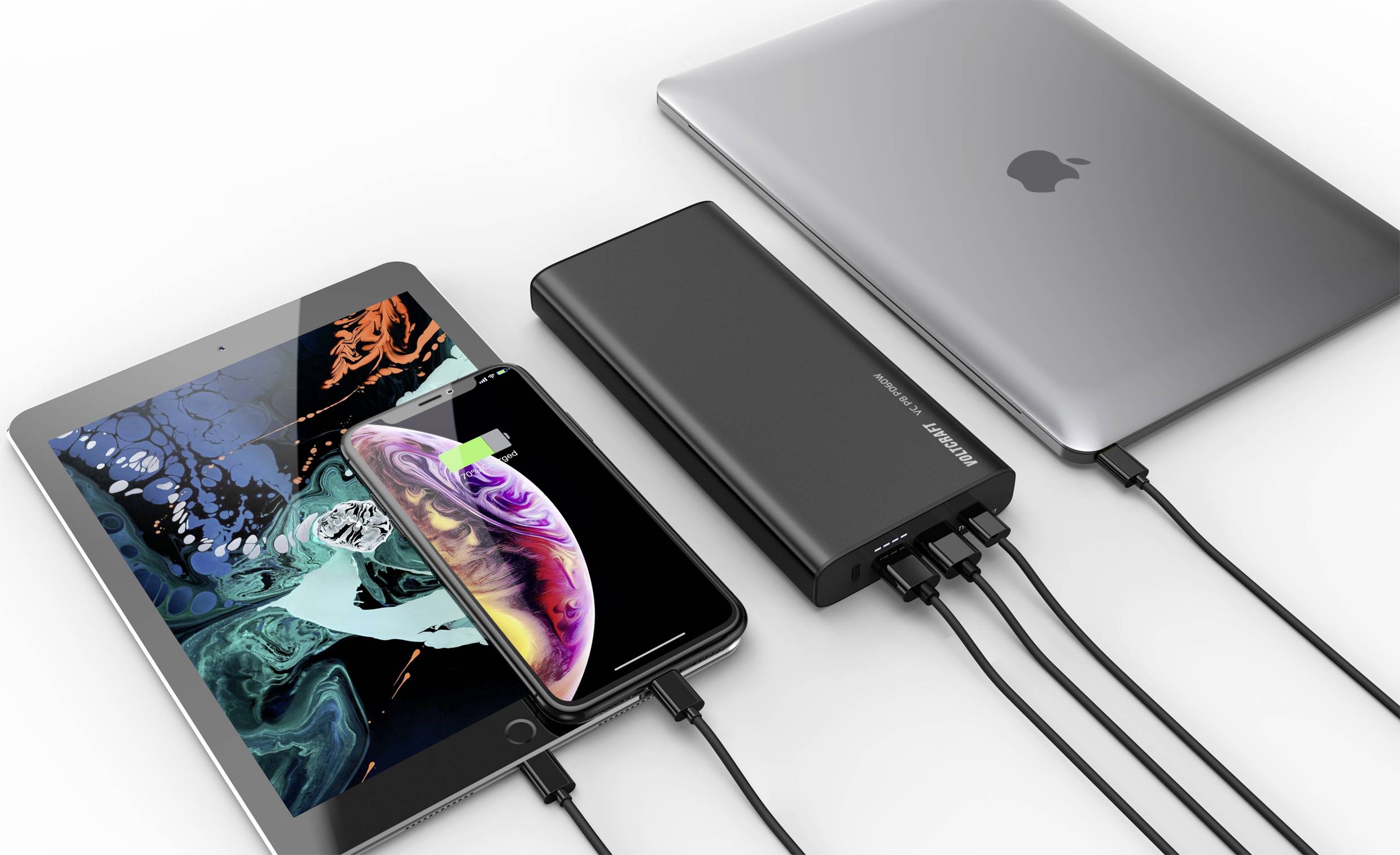 A tablet, smartphone and laptop are being charged simultaneously via a black charger with multiple USB cables.