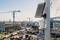 Surveillance and solar installation on a mast in front of a large construction site with cranes and building structures in the background.