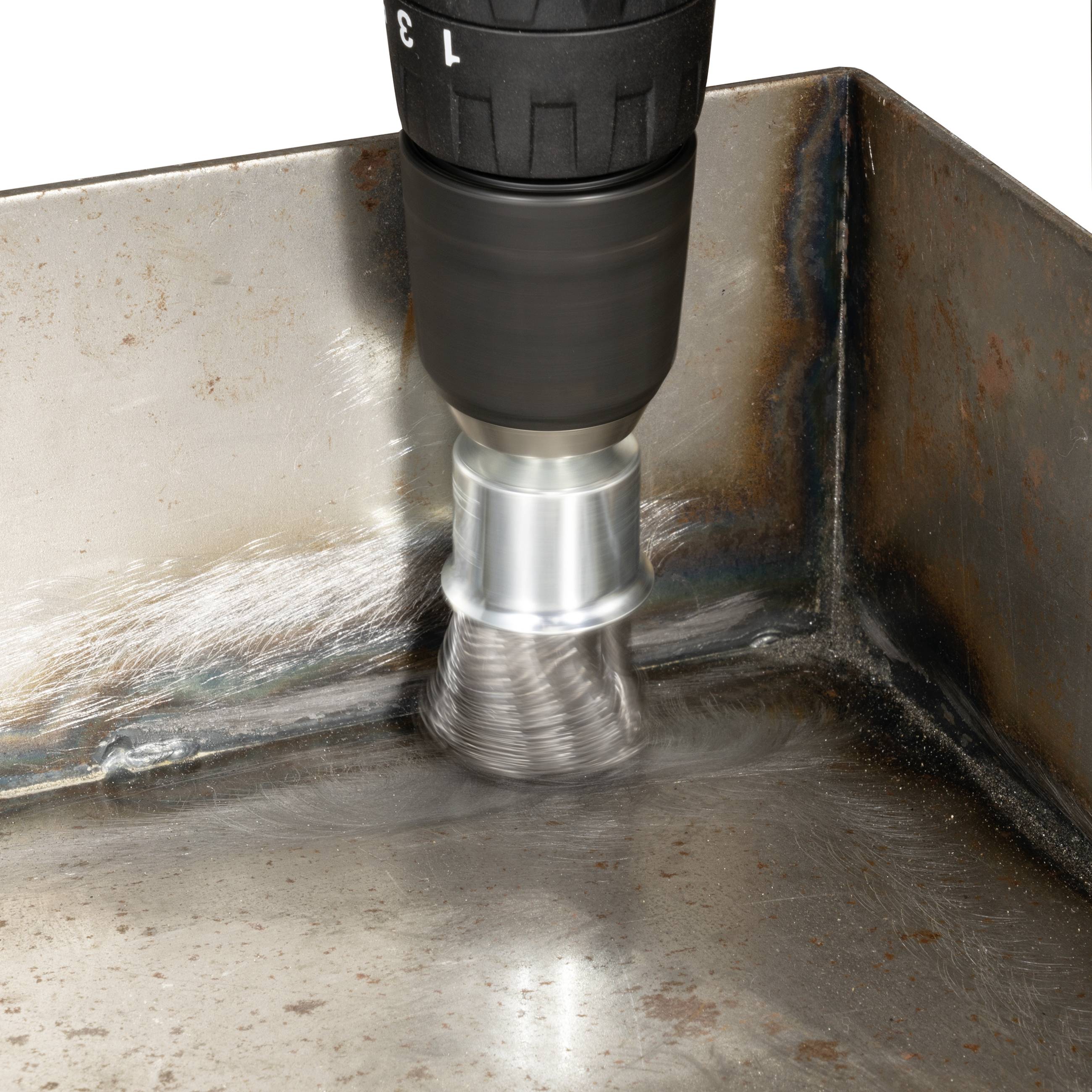 A round wire brush on an angle grinder is polishing a metal surface in a corner.