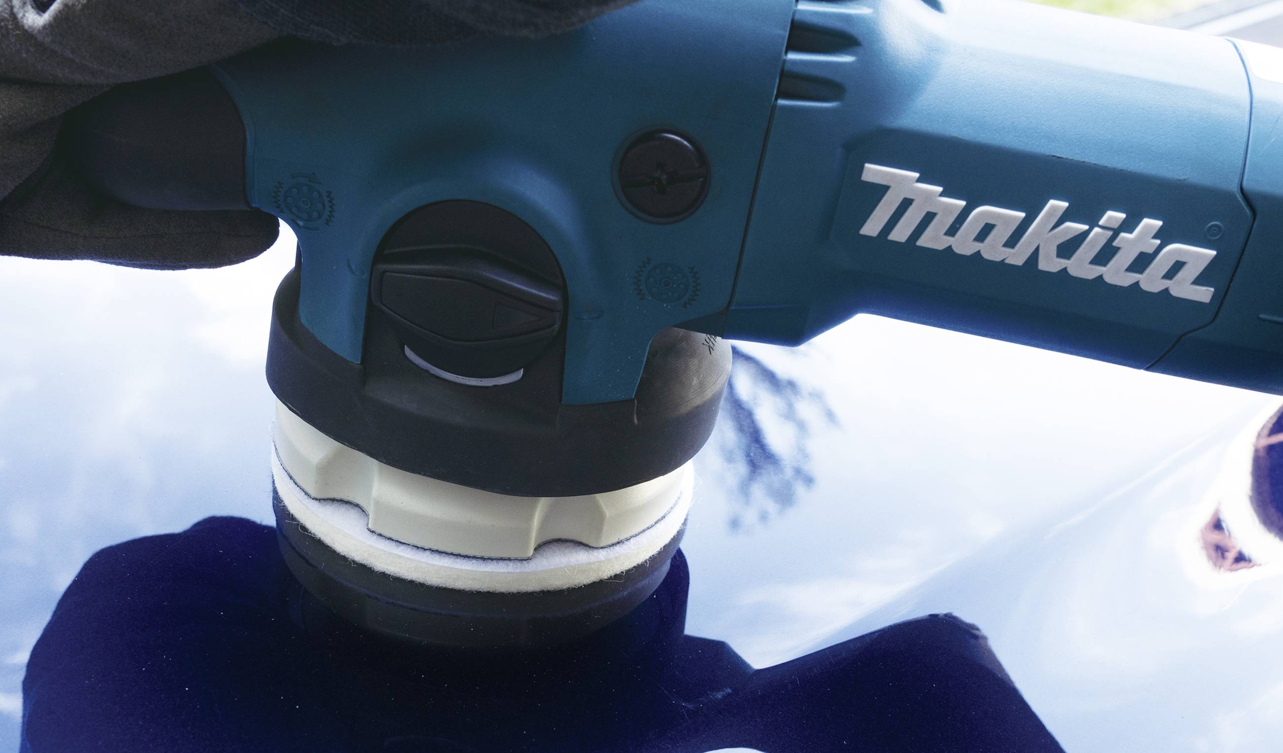 A person is polishing the surface of a car with a blue Makita electric polishing machine.