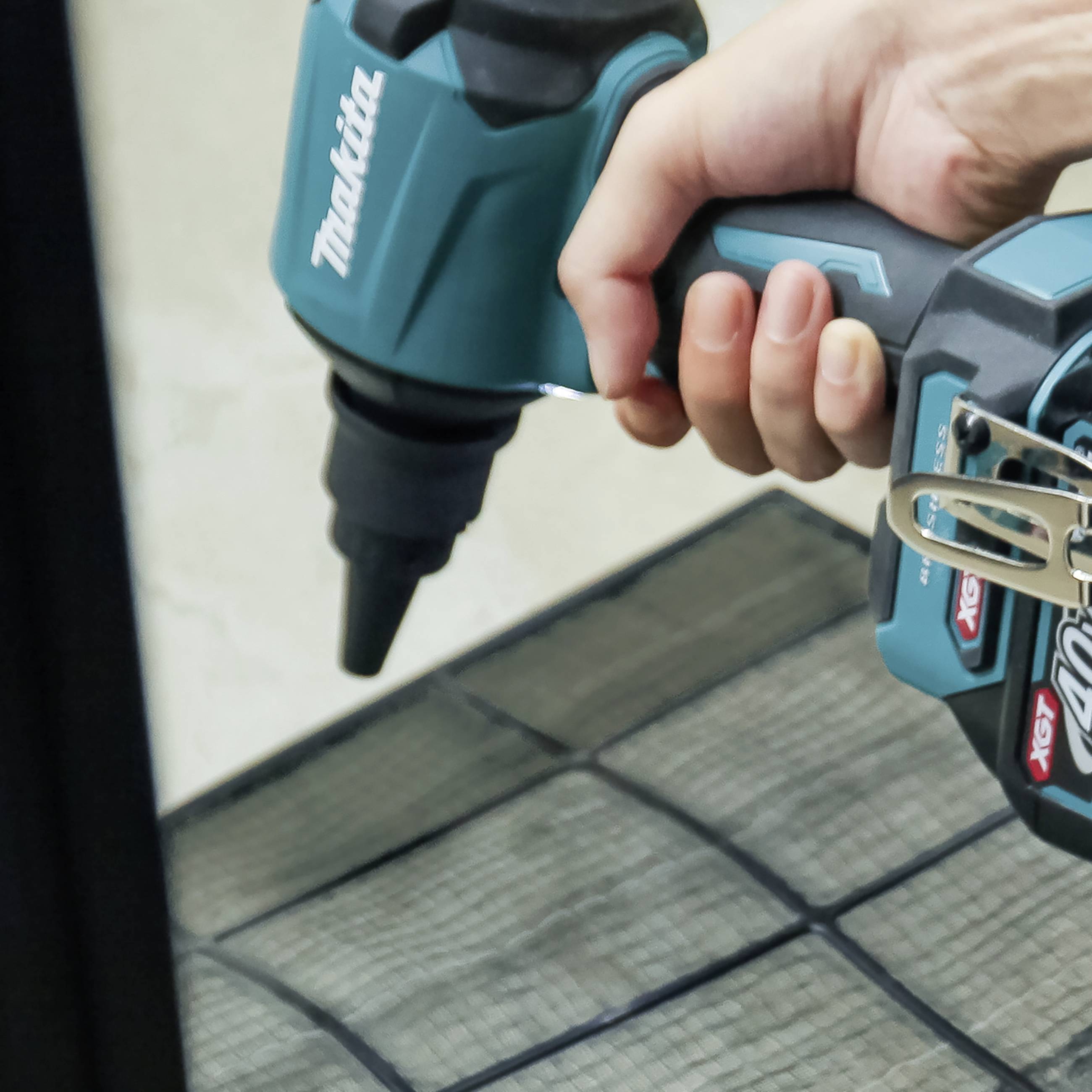 A hand is holding a blue power drill pointing at a black wire fence.