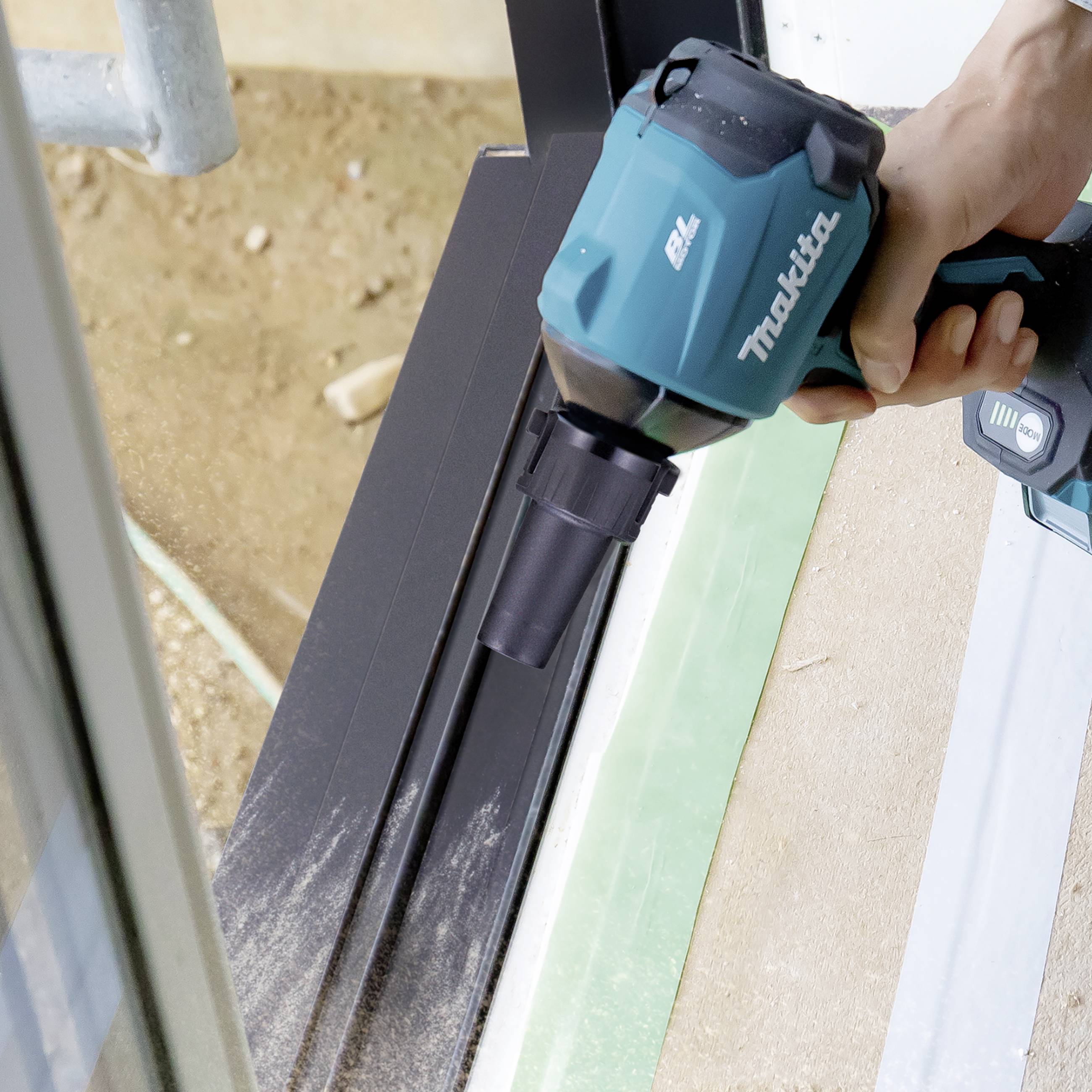 A person is using a cordless vacuum cleaner by Makita to clean a metal frame.