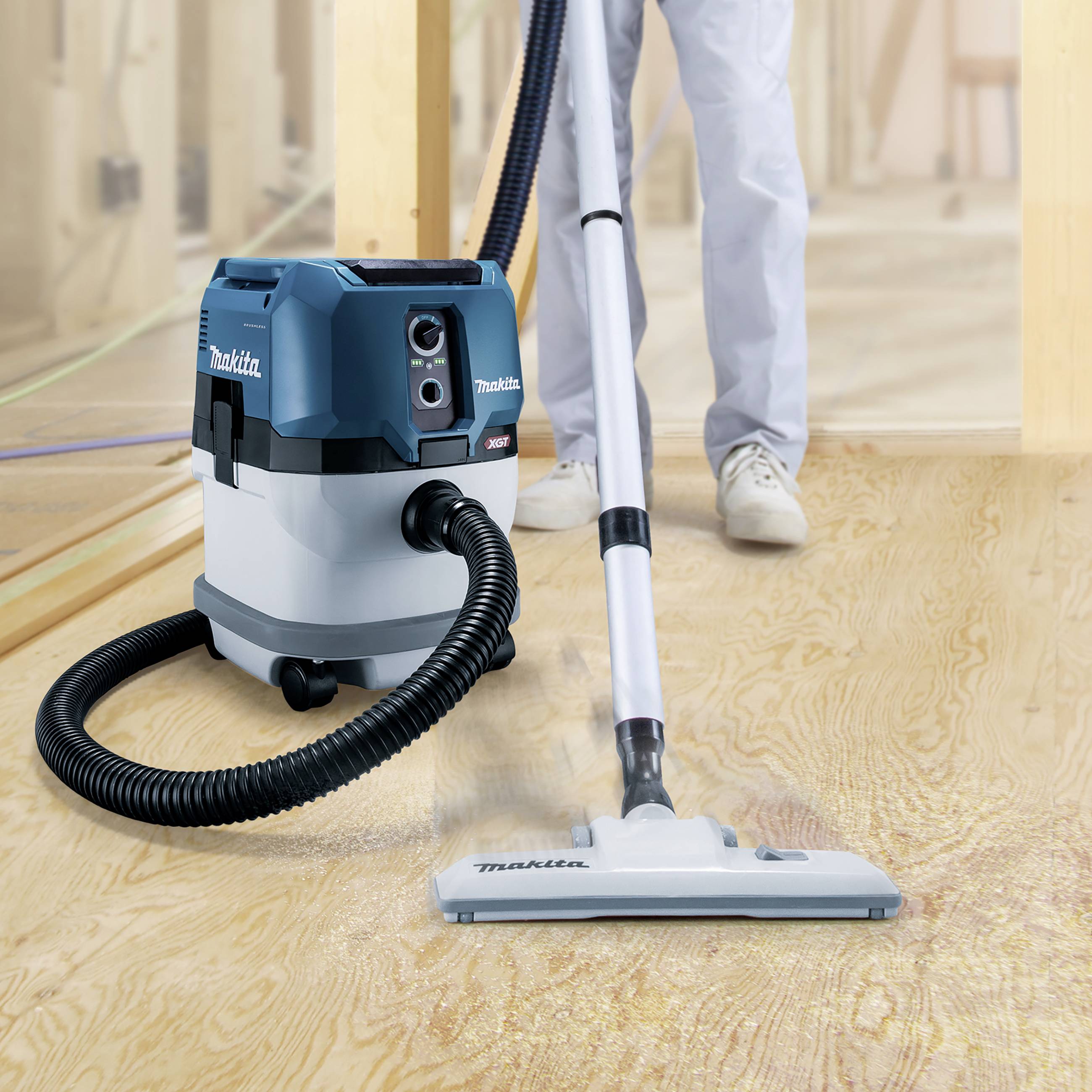 A person is vacuuming a wooden floor with a vacuum cleaner. The vacuum cleaner is blue and white and fitted with a long hose.