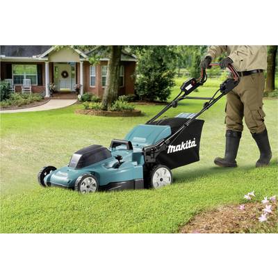 A Makita lawnmower is being used by a person on a well-maintained lawn in front of a house.