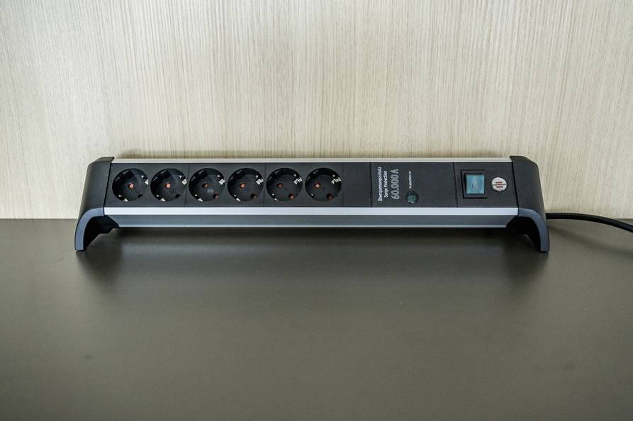 Six-way extension socket with surge protection and switch, sitting on a table, in front of a wooden panel.