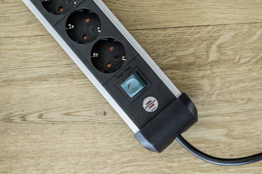 A multi-socket extension lead with several plug sockets and a blue power switch, resting on a wooden floor.