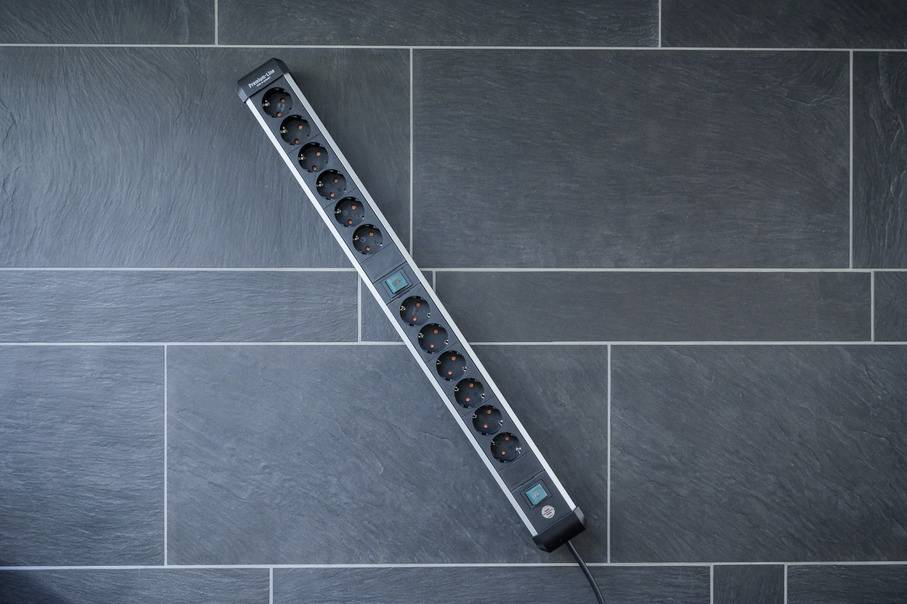 Multi-socket extension with ten sockets and circuit breaker, diagonally placed on grey flooring.