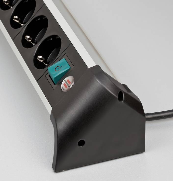 A black power strip with five sockets and a green on/off switch against a grey background.