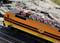 Toy model of a yellow and black electric locomotive with a detailed view of the overhead line, positioned on tracks against a rocky background.