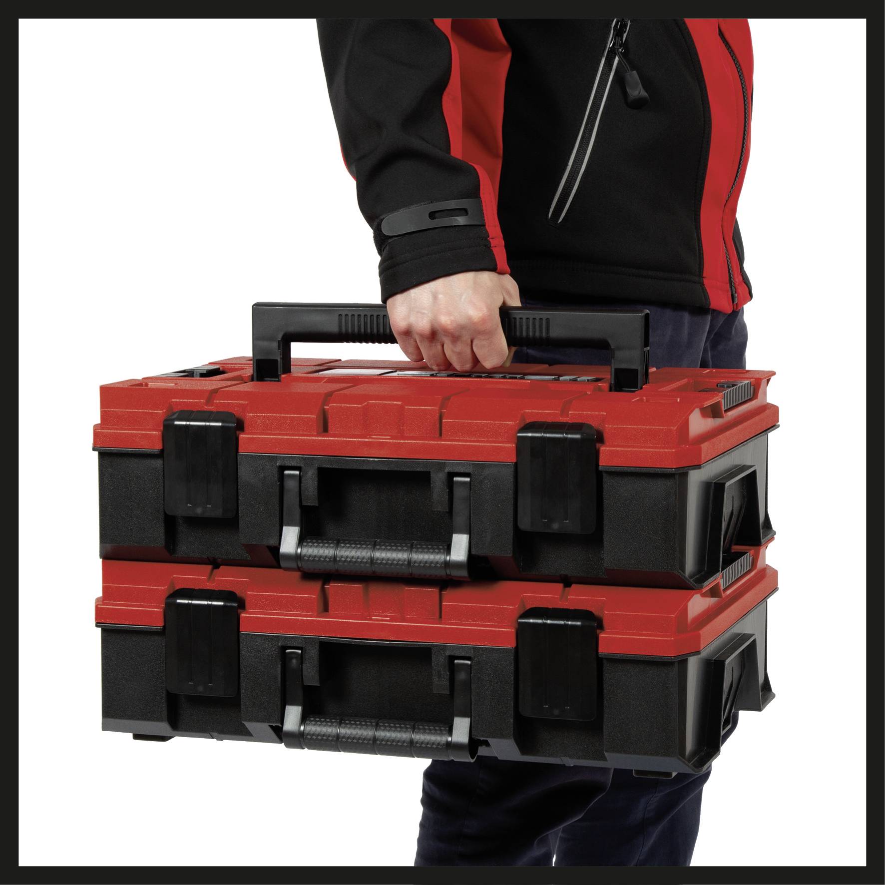 A person is carrying two stacked, red and black tool cases by their handle.