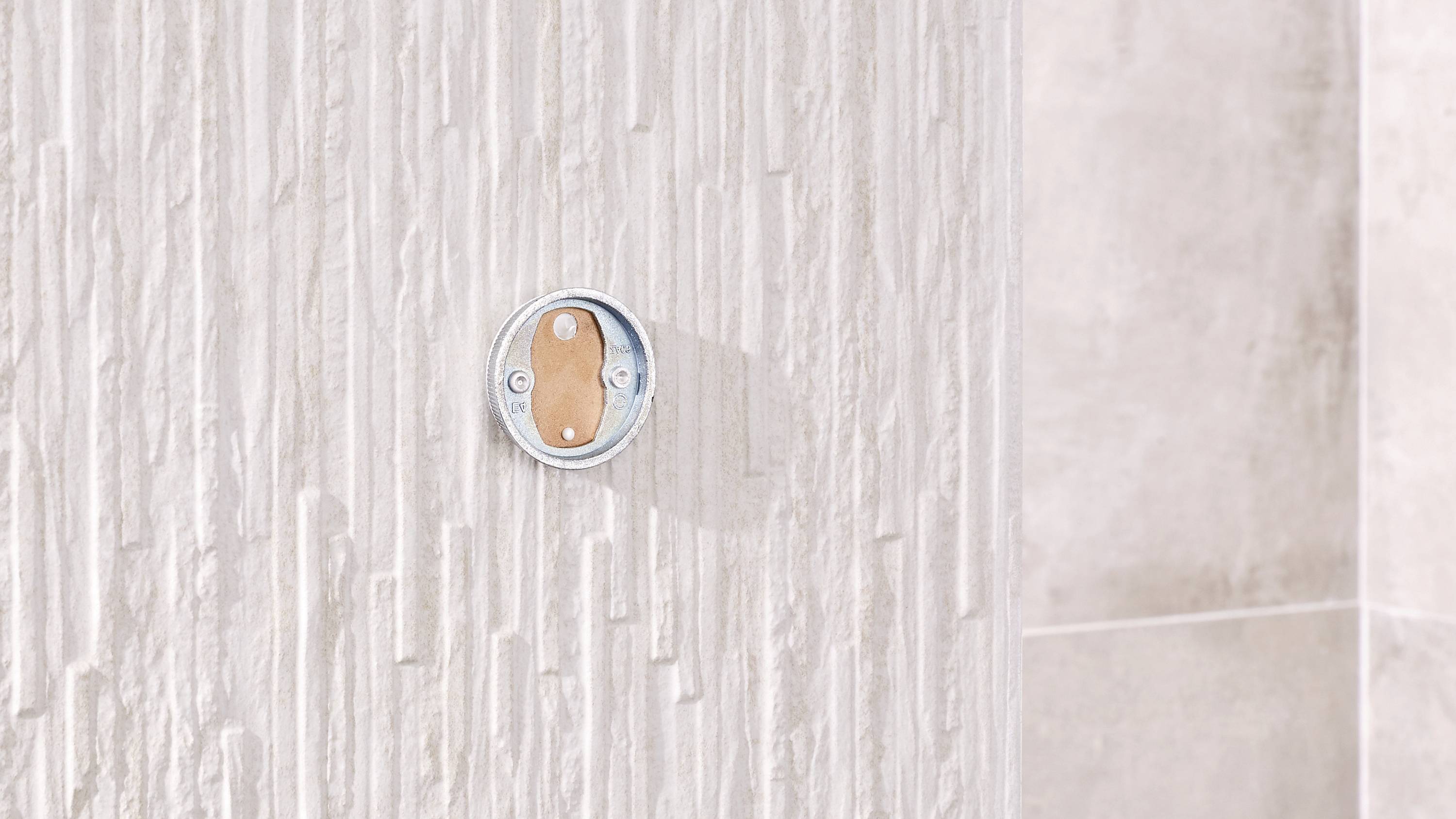 Cylindrical object with screws against a beige, textured wall.