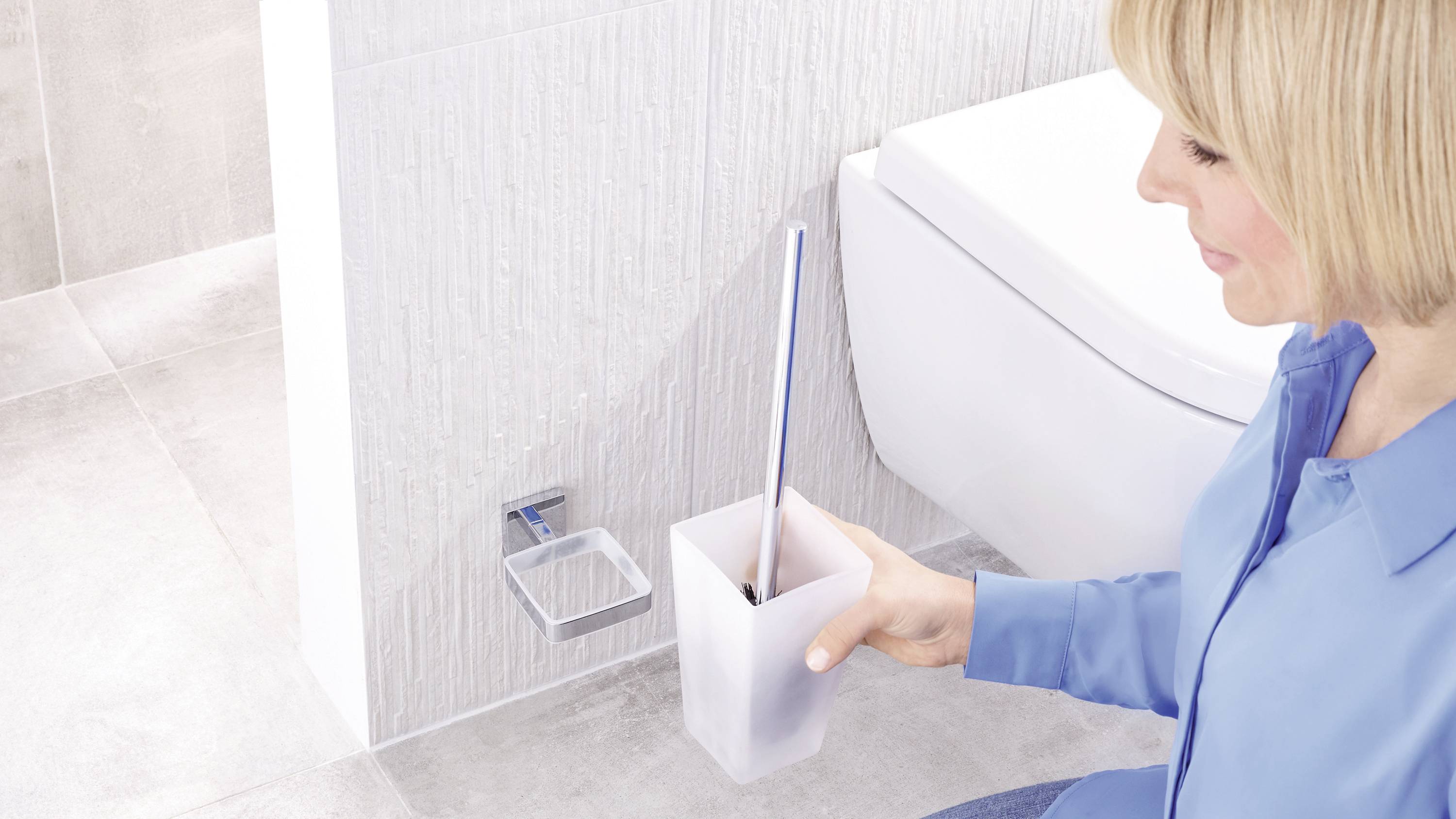 A person is cleaning the bathroom with a toilet brush. The white toilet is visible in the background.