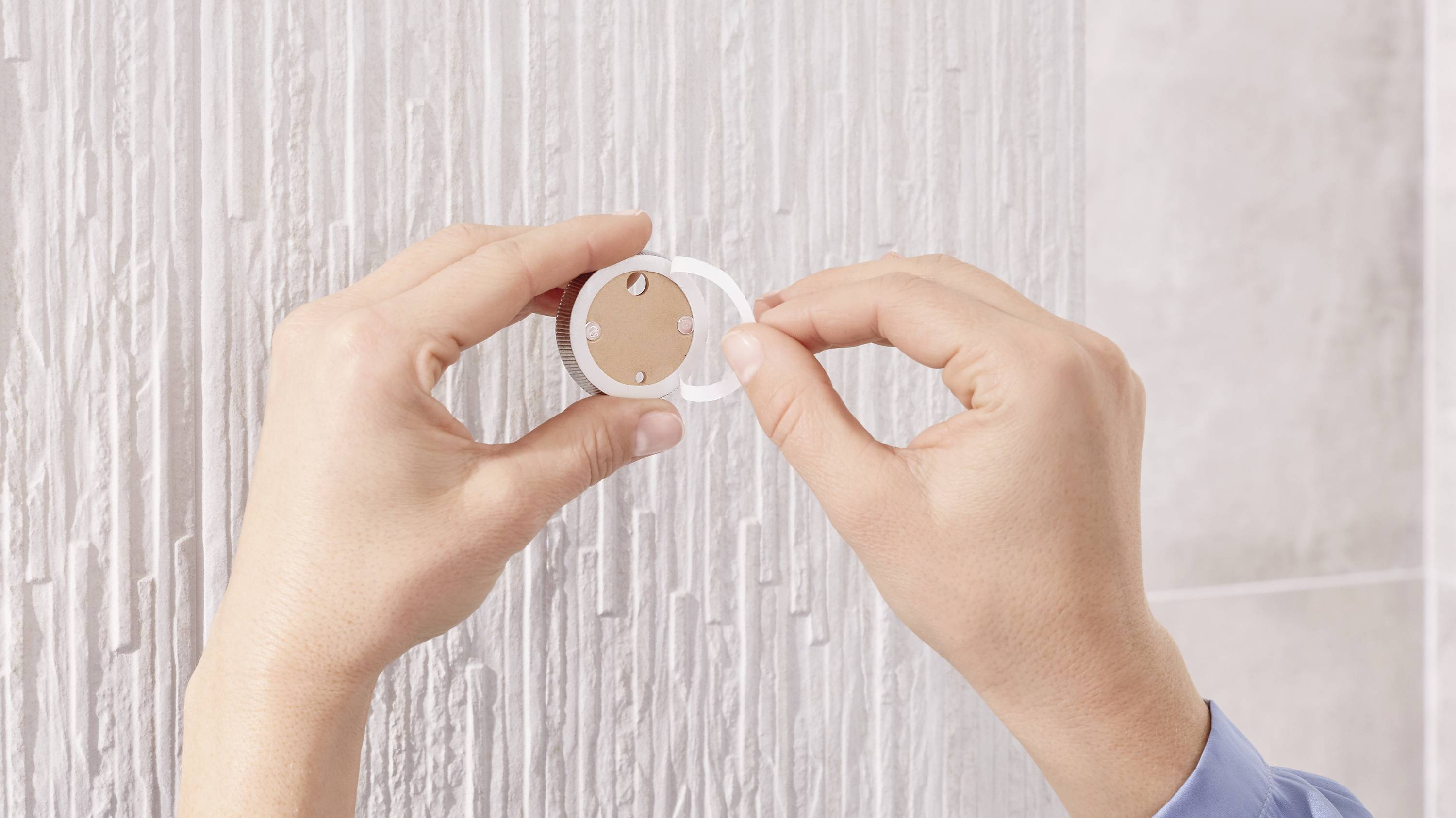 A person is hanging a round, white wall clock on a textured white wall.