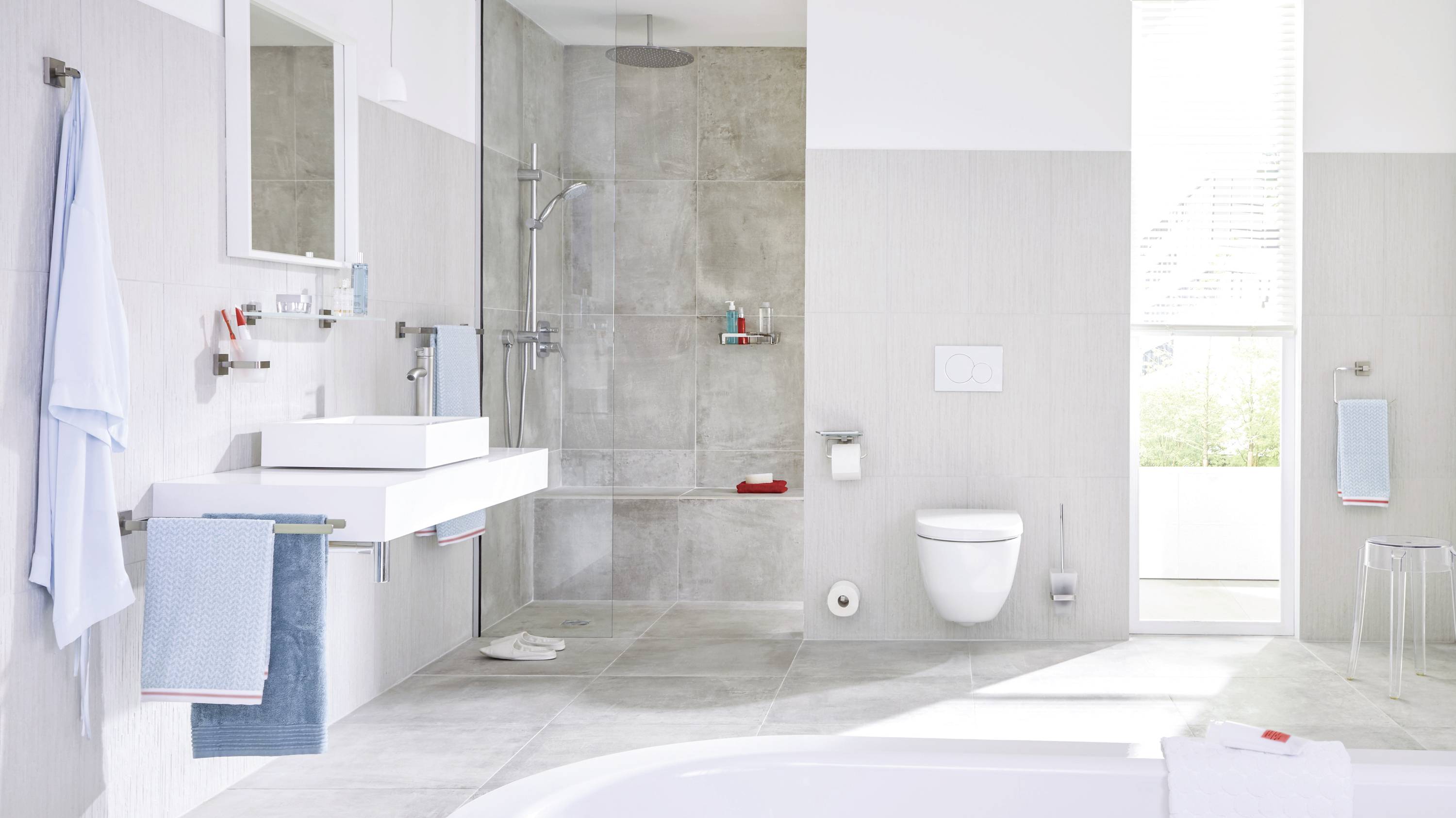 Modern bathroom with grey tiles, shower, washbasin, toilet and towels in blue and white tones. Bright and clean atmosphere.