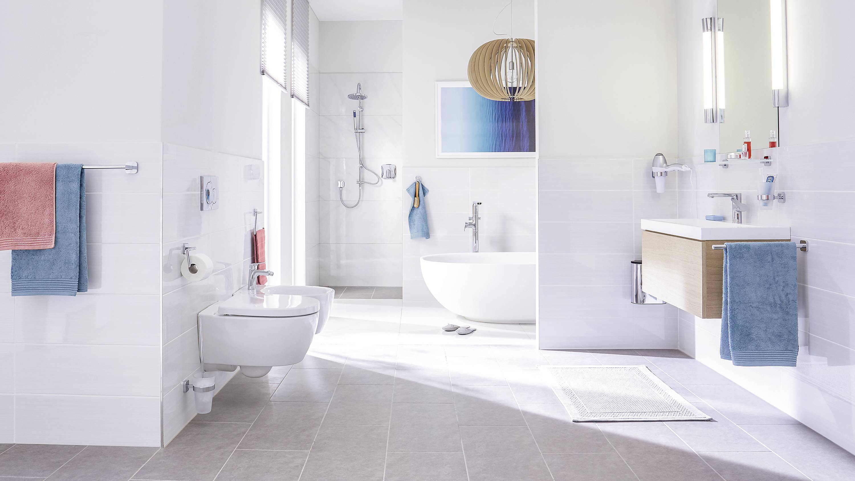 Spacious, modern bathroom with a freestanding bath, washbasin, shower and towels in various colours.