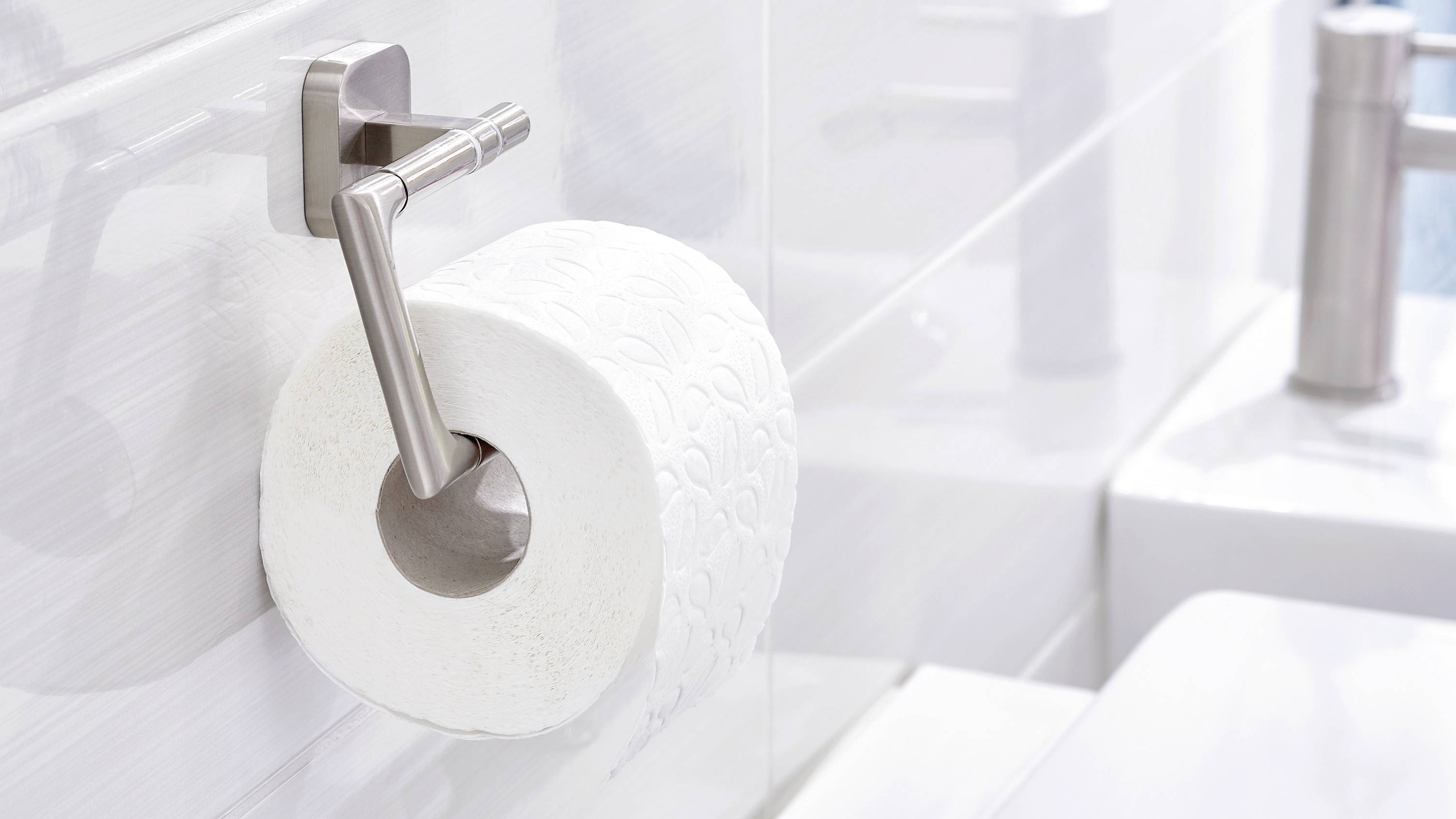 Toilet roll on a holder attached to a white bathroom wall, next to a sink.