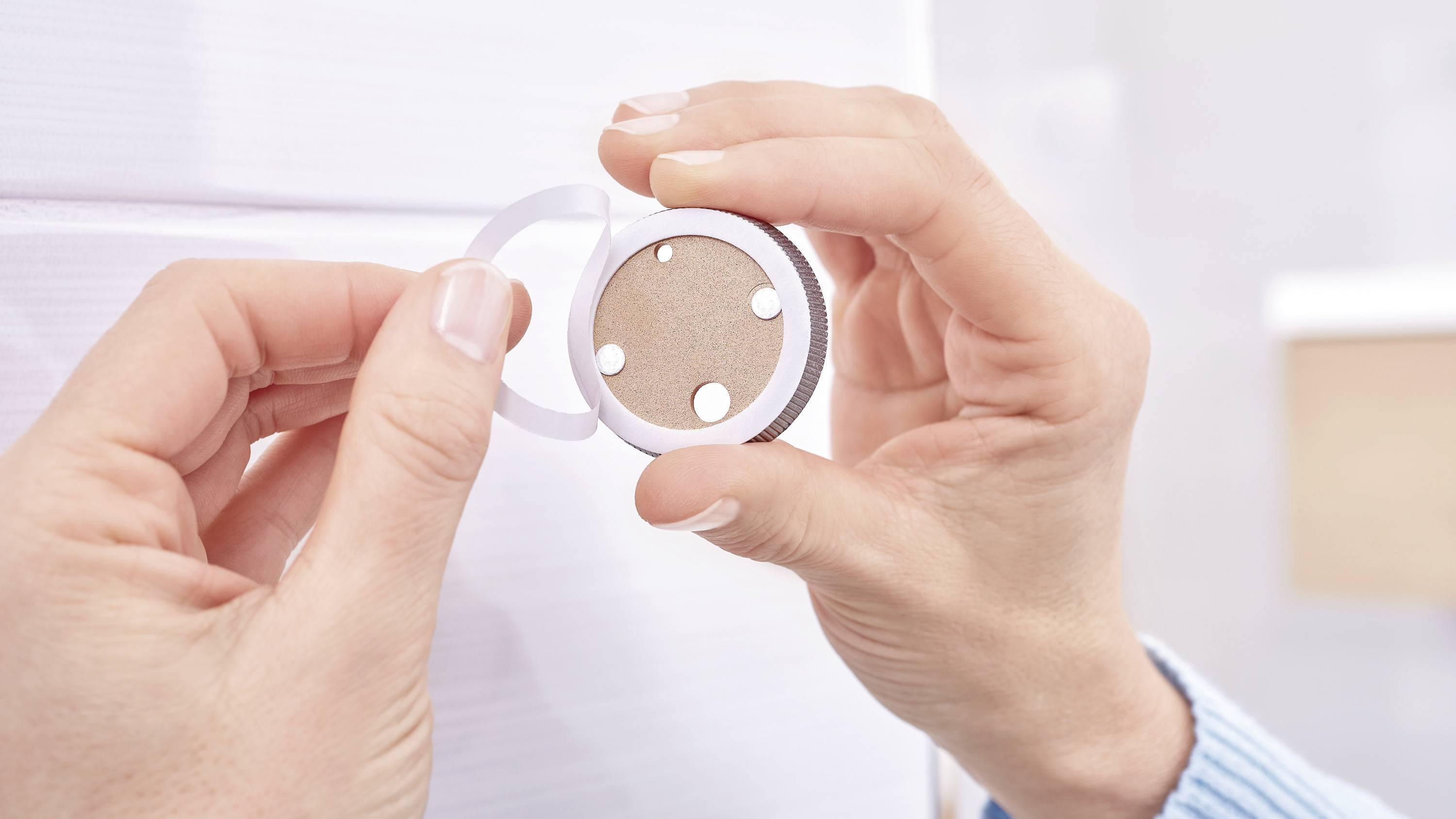 A person is attaching a circular sticker to a wall or surface. The sticker has several white dots.