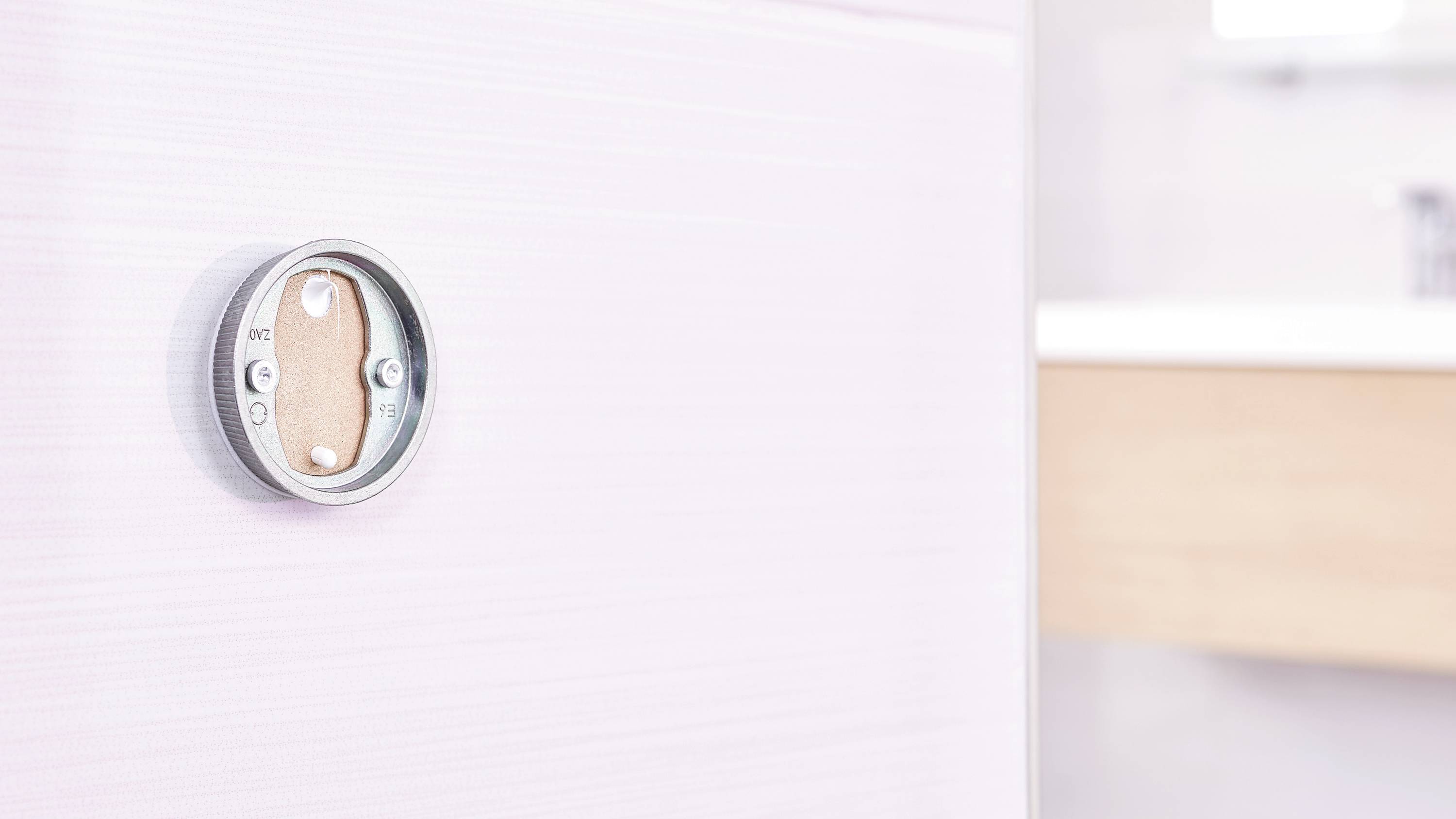 A round thermostat on a beige wall in the bathroom. It is modern in design and blends harmoniously into the surroundings.