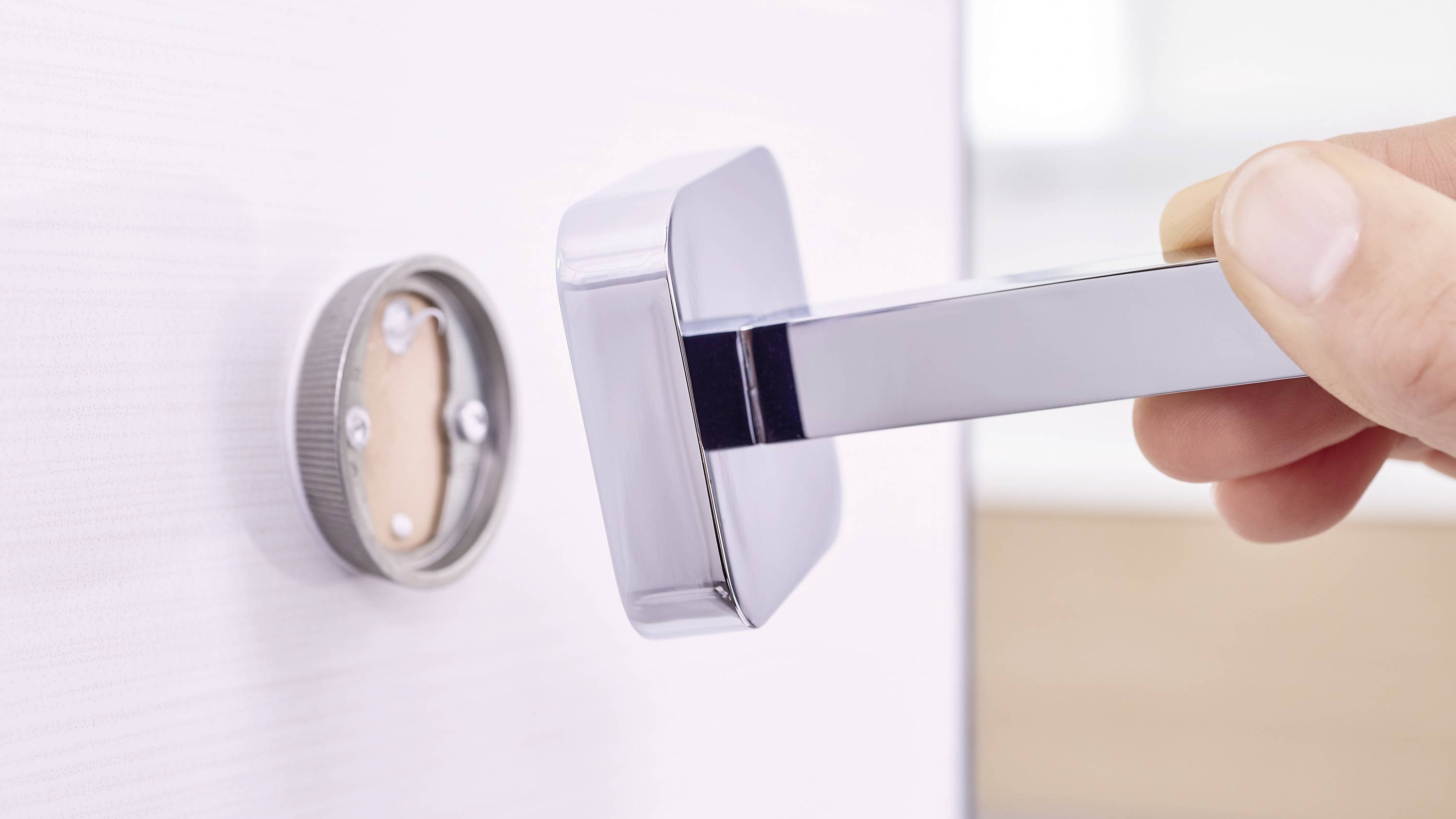 A hand turns a modern door handle on a white wooden door. Focus on the shiny metallic handle and the locking mechanism.