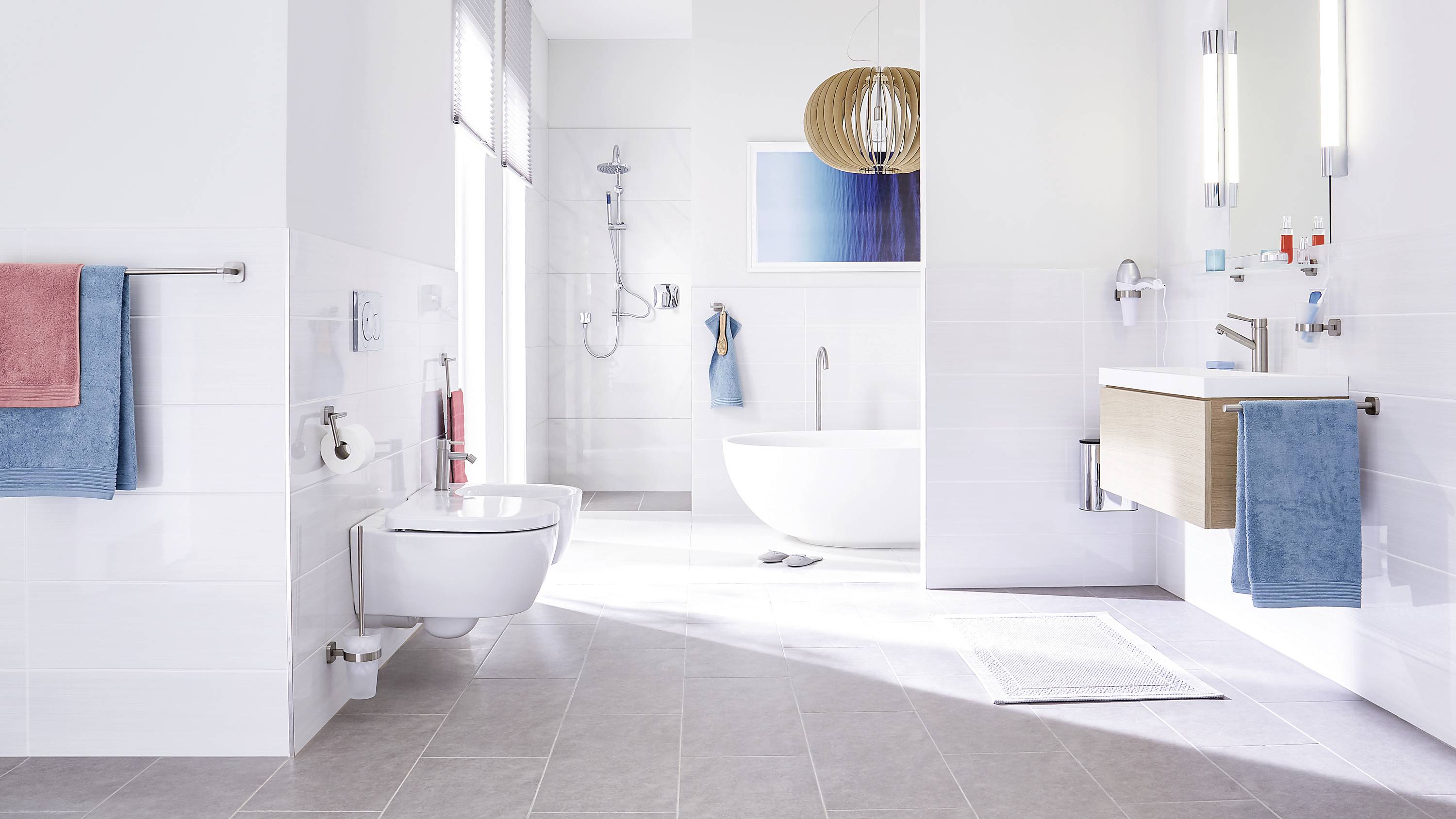 Bright bathroom with a freestanding bathtub, wall-mounted washbasin, toilet, bidet, and coloured towels on the towel rails.