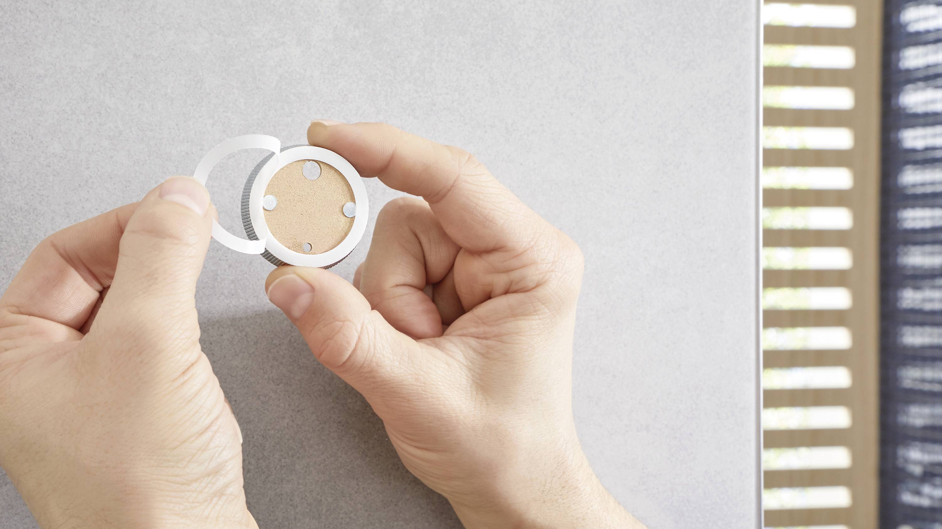 Two hands hold an empty powder compact against a grey background.