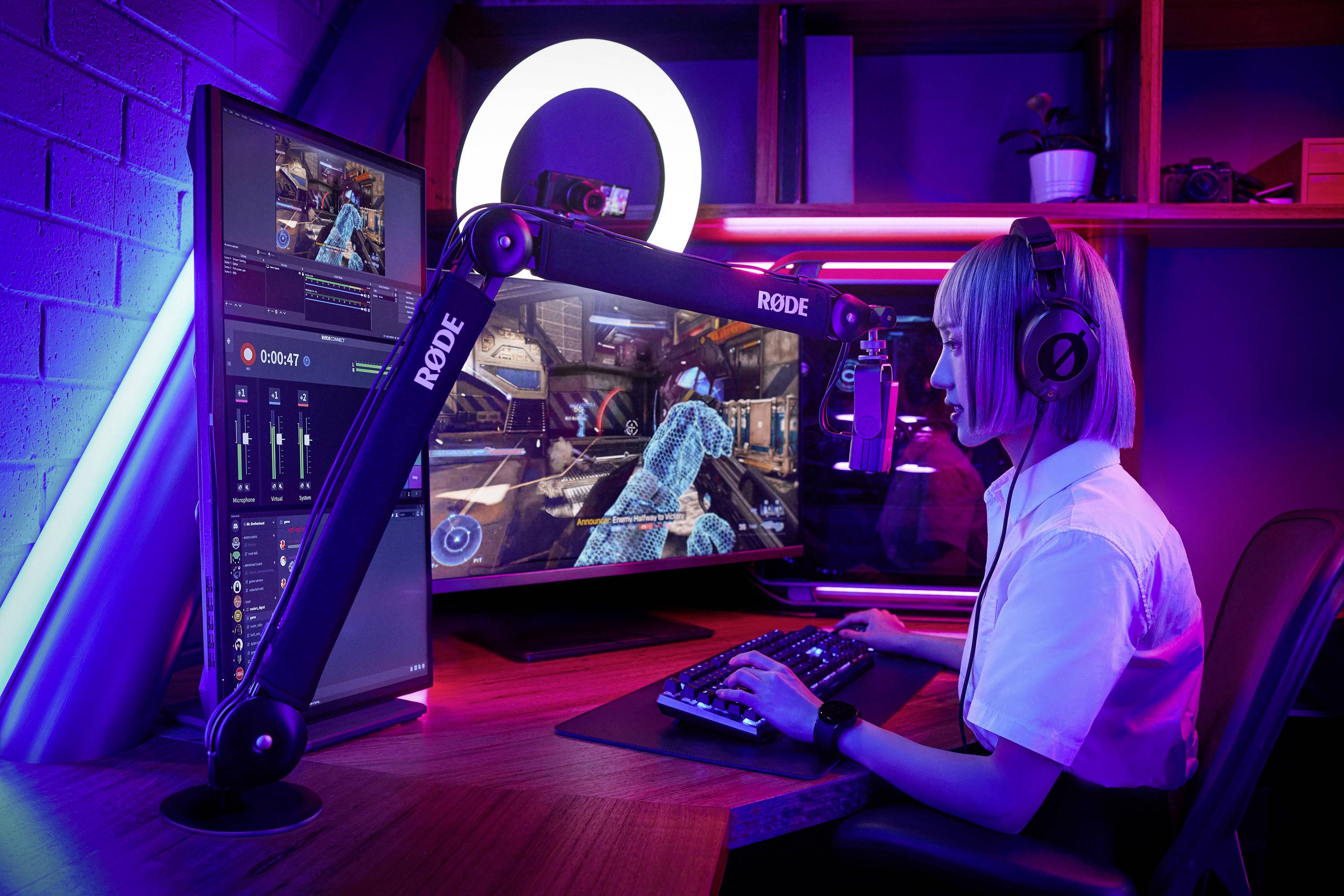 A woman is playing a video game on a computer with multiple monitors in a room with colourful lighting. She is wearing headphones.