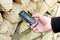 A hand holds a moisture metre against a stack of chopped firewood to measure its moisture content.