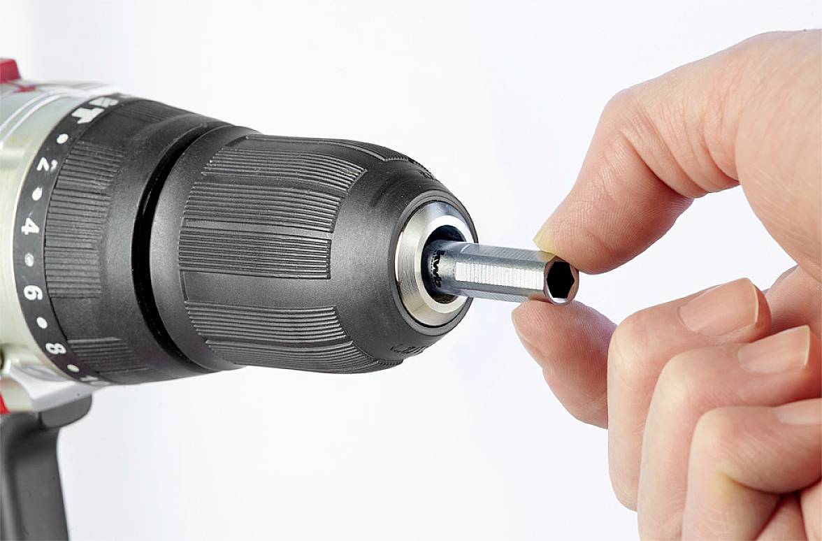 A hand is holding a screwdriver bit being inserted into an electric drill chuck.
